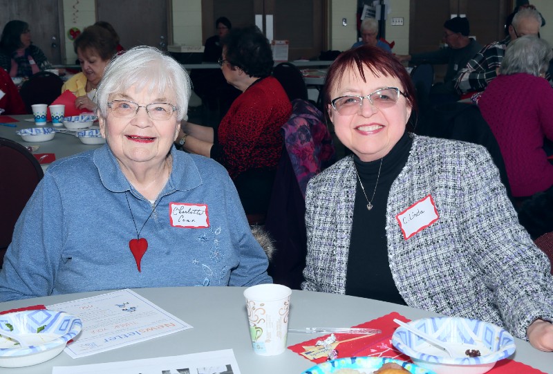 Two older women smile, sitting together at table.